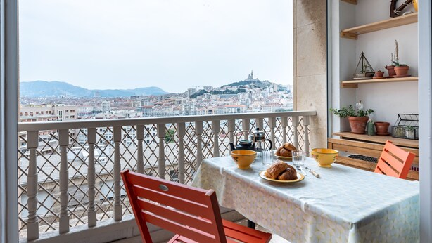Un balcon avec une table dressée pour le petit-déjeuner, offrant une vue sur le paysage urbain et une colline imposante.
