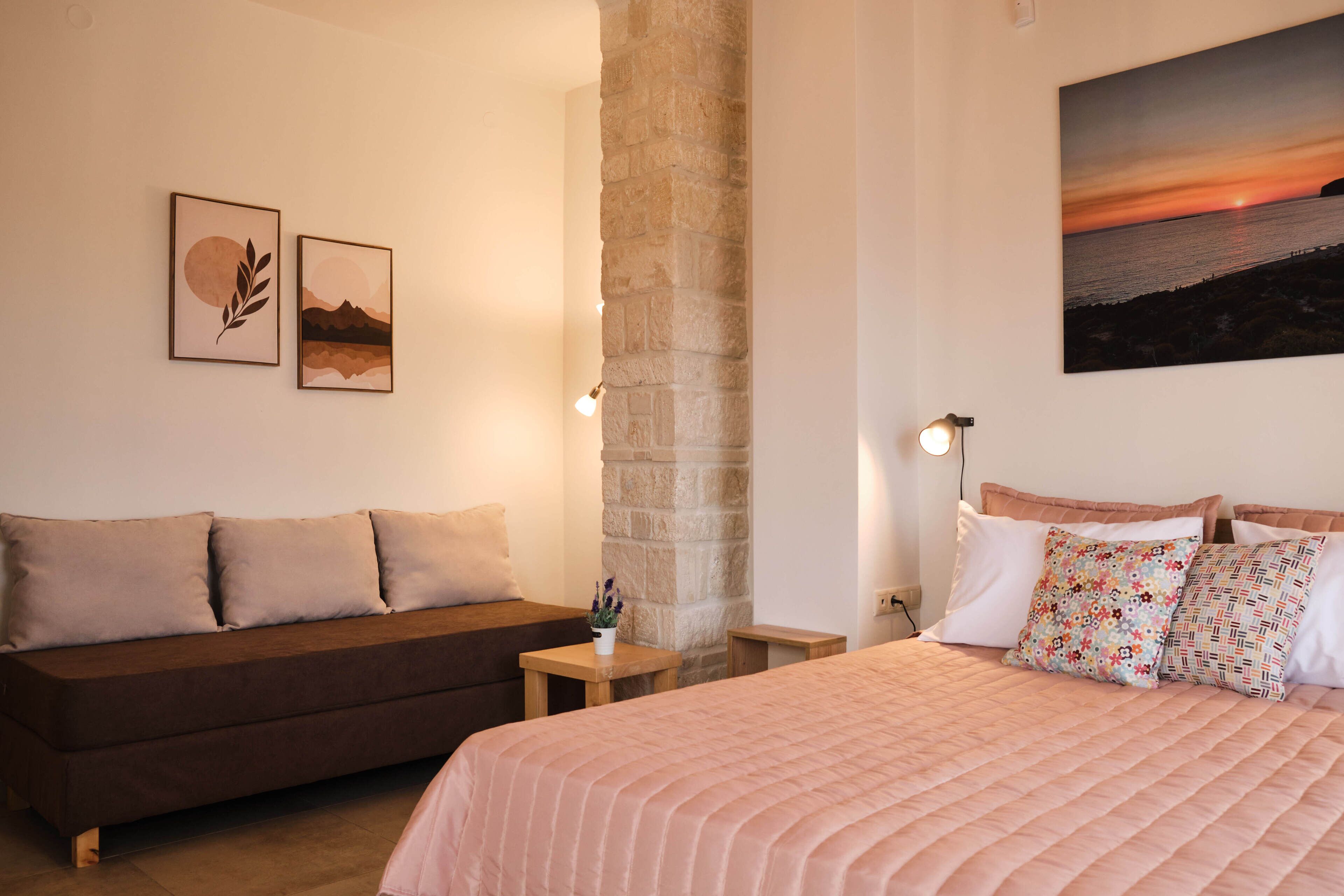 Ein Schlafzimmer mit Bett, Sofa, Nachttisch, Lampe und Kunstwerken an den Wänden.