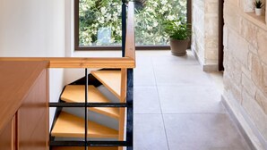 Un escalier avec des marches en bois et des rampes noires, menant à une pièce dotée d’un mur en pierre et d’une fenêtre donnant sur un jardin fleuri.