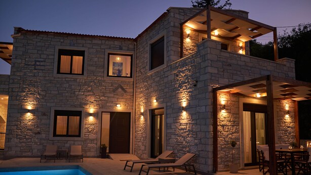Une maison en pierre à deux étages, dotée d’une piscine, d’un espace salon extérieur et d’un patio.