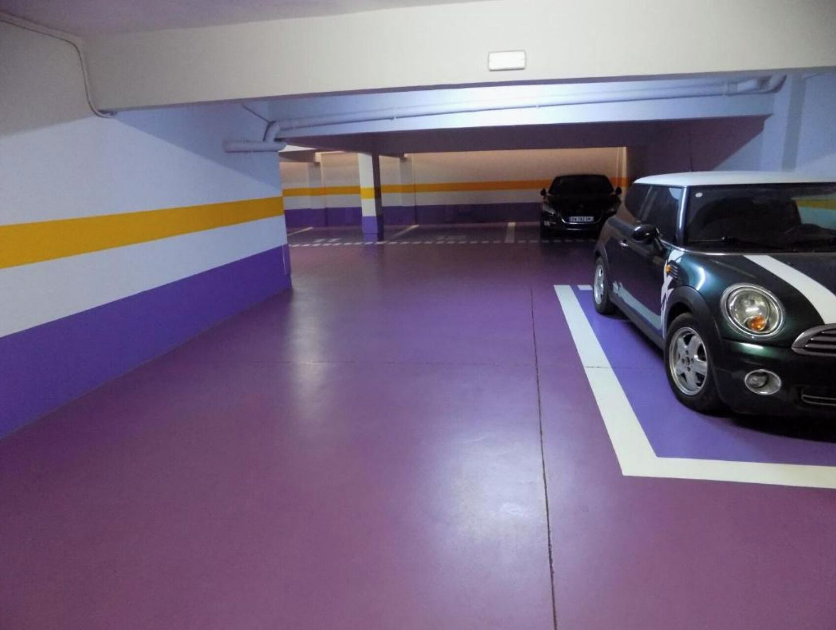 A parking garage with purple and yellow striped walls and a black car parked in a designated space.