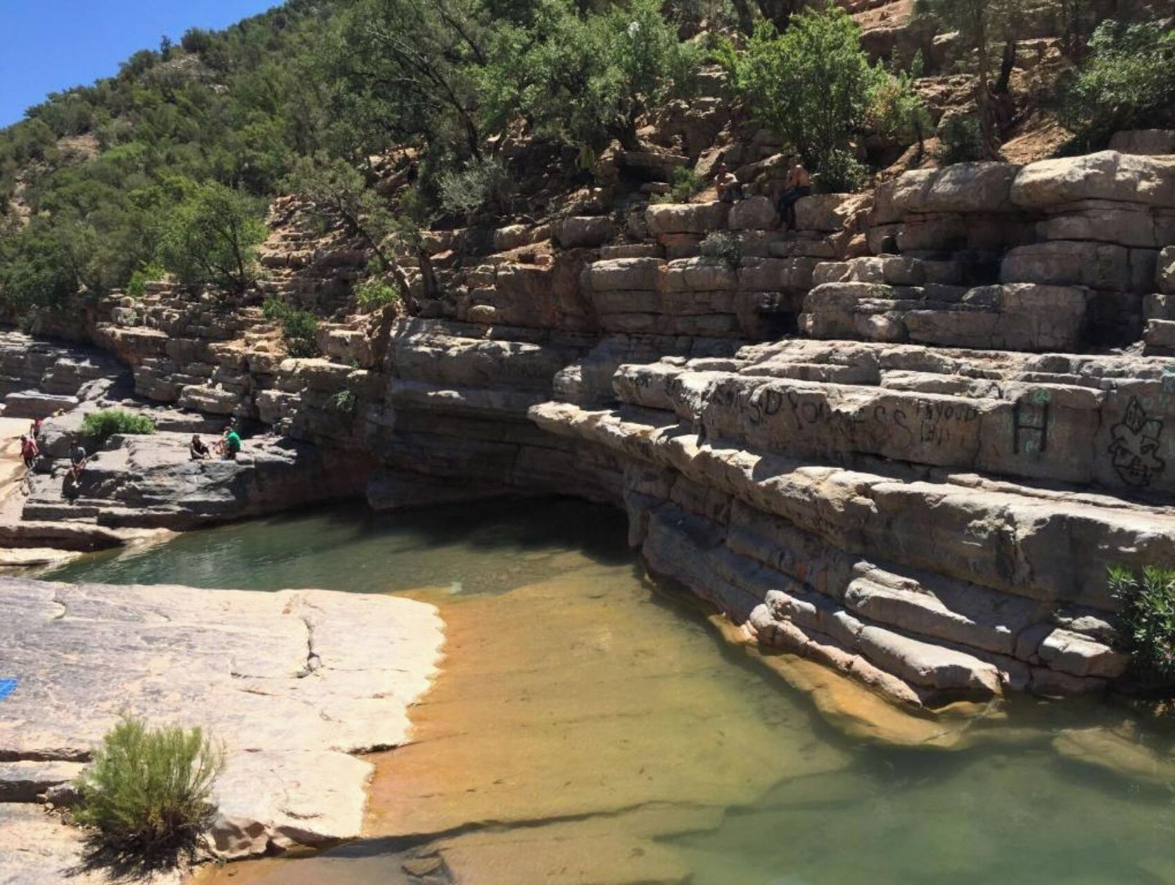 Paisagem rochosa e natural com um lago límpido rodeado por penhascos e vegetação rasteira.