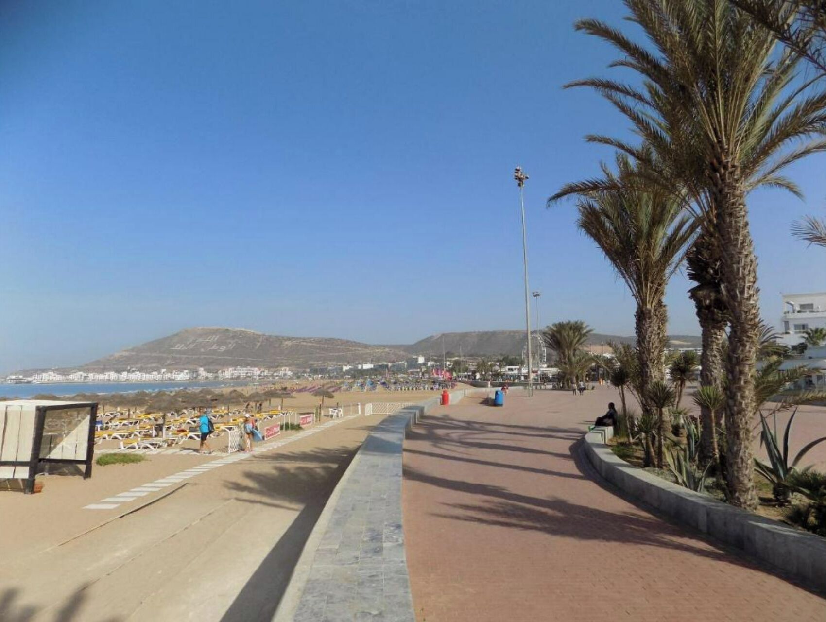 A coastal promenade with a clear view of the beach and a mountain in the distance.