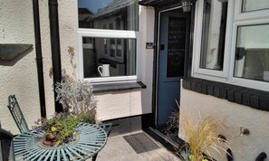 A building entrance with a window, a door with a chalkboard sign, and a small table with potted plants. - Cosy, Spacious 2-bed Cottage in Watchet, Somerset (Watchet)