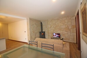 A living room with a stone wall, a fireplace, a TV, and a glass dining table.
