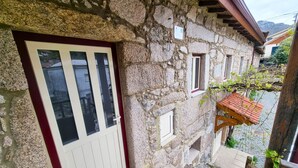 A stone building with a red door, small windows, and a wooden balcony with a tiled roof. - rural house in Geres for 4 people with fireplace (Gerês)