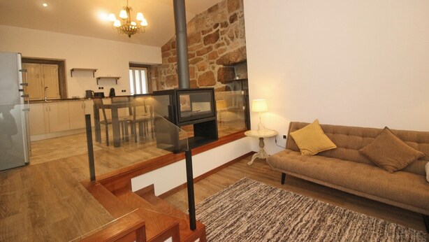 A modern living room with a stone wall, a fireplace, a sofa, and a glass table. - rural house in Geres for 4 people with fireplace (Gerês)