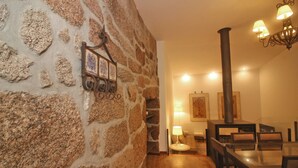 A stone-walled dining area with a wooden table and chairs, a hanging light fixture, and a fireplace. - rural house in Geres for 4 people with fireplace (Gerês)