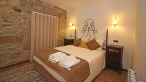 A bedroom with a stone wall, a bed with a brown bedspread, two bedside tables with lamps, and a window with blinds. - rural house in Geres for 4 people with fireplace (Gerês)