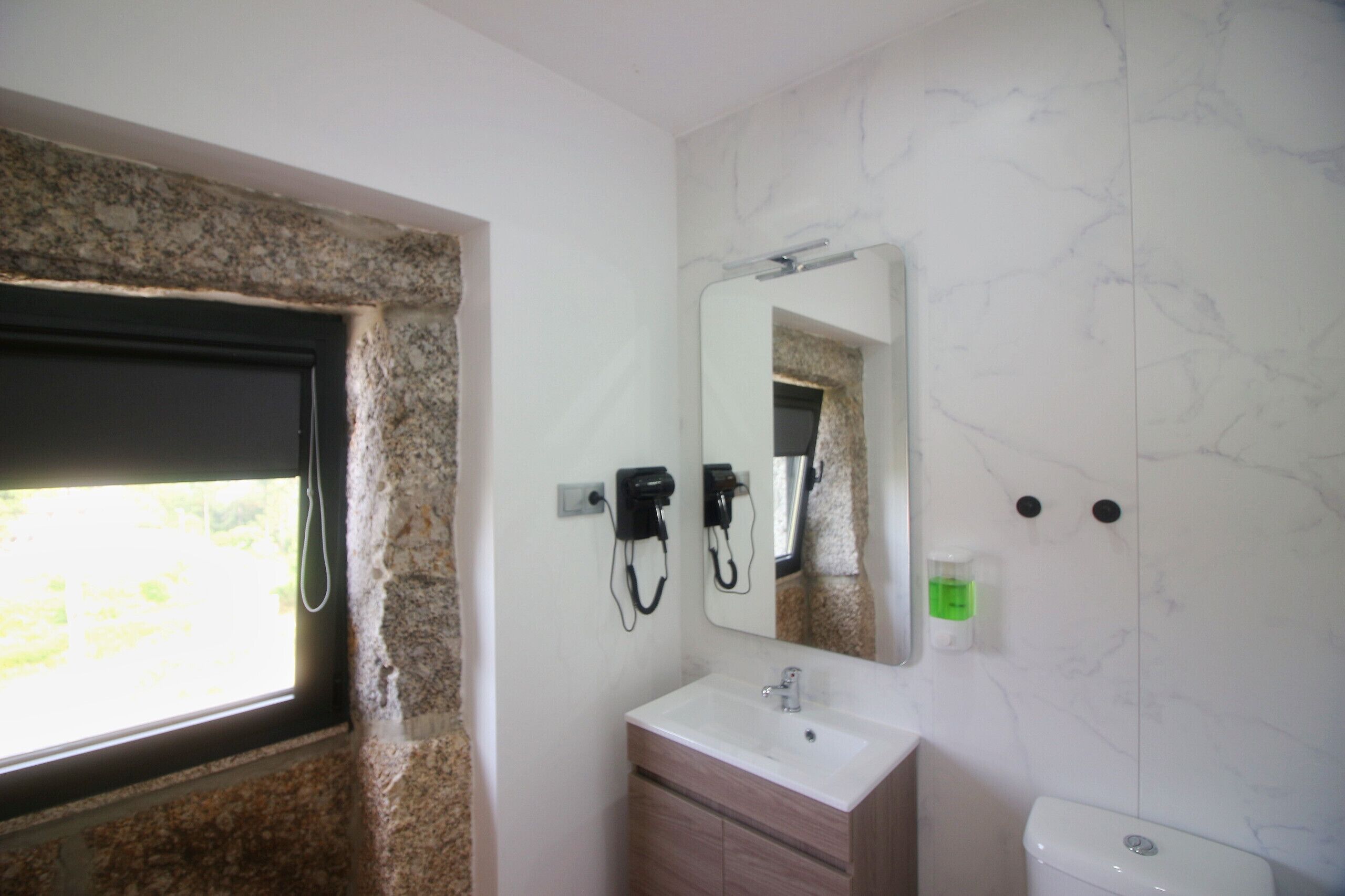 Un baño con pared de piedra, ventana, lavamanos, espejo y retrete.