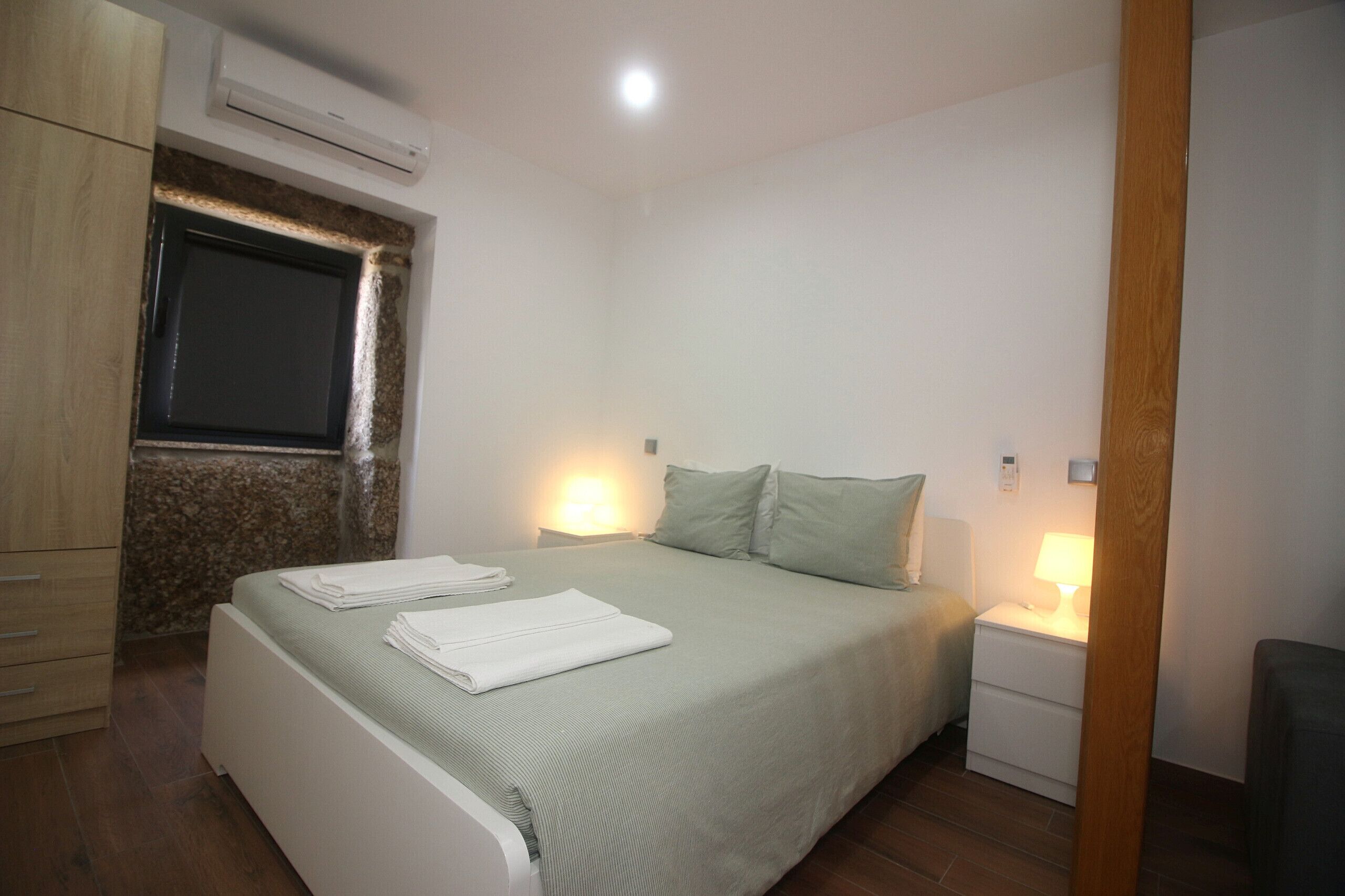 Un dormitorio con cama, mesitas de noche, una ventana y un equipo de aire acondicionado.
