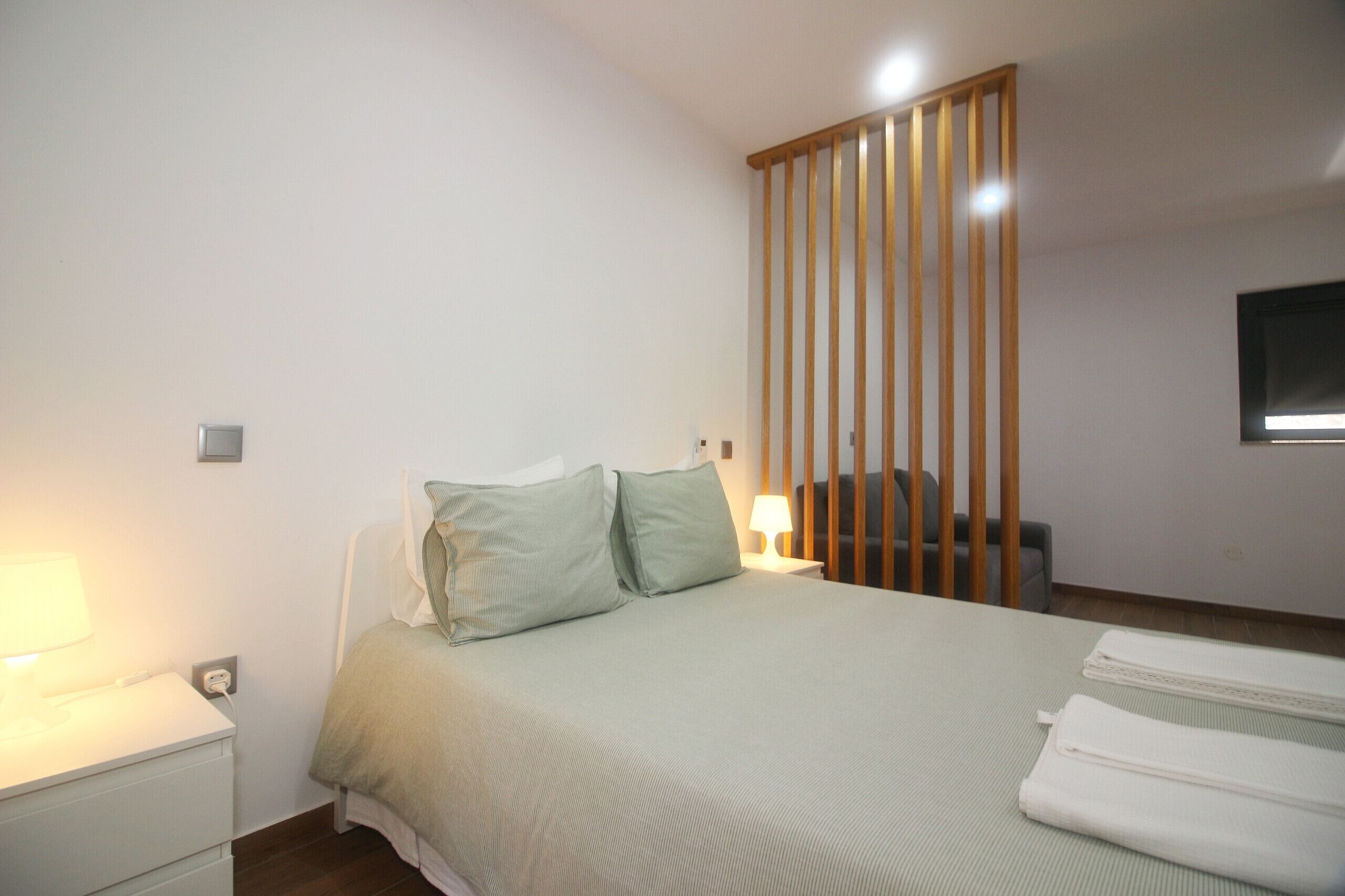 A hotel room with a bed, a nightstand, a lamp, a wooden partition, and a television on the wall.
