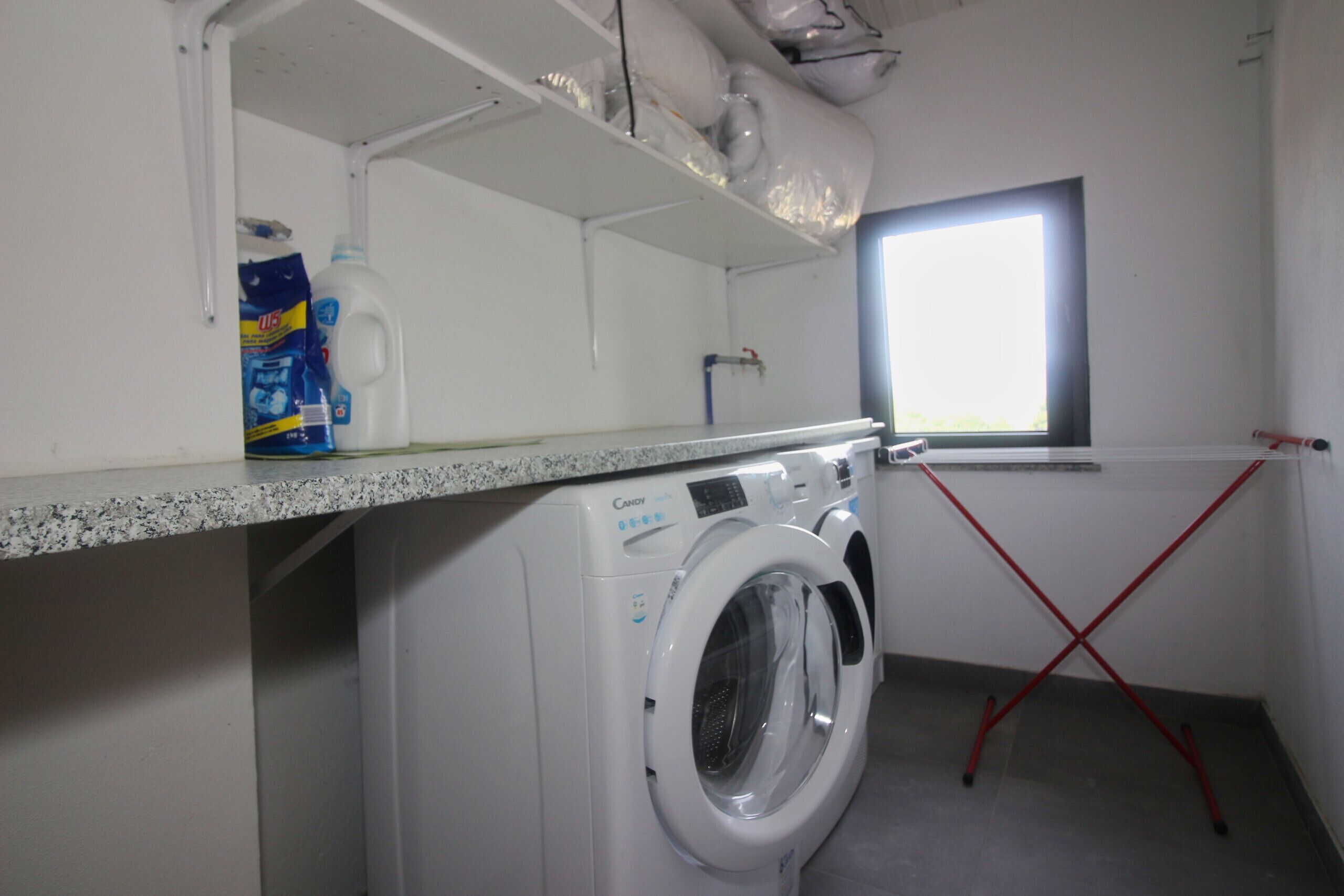 A laundry area with a washing machine, a detergent bottle, and a window.