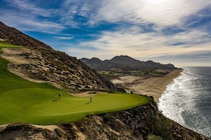 Un campo de golf costero con vistas al océano y a las montañas.