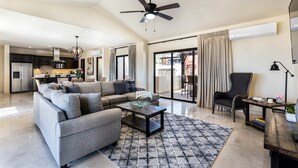 Ein geräumiges Wohnzimmer mit grauem Ecksofa, einem Couchtisch und einem Deckenventilator.