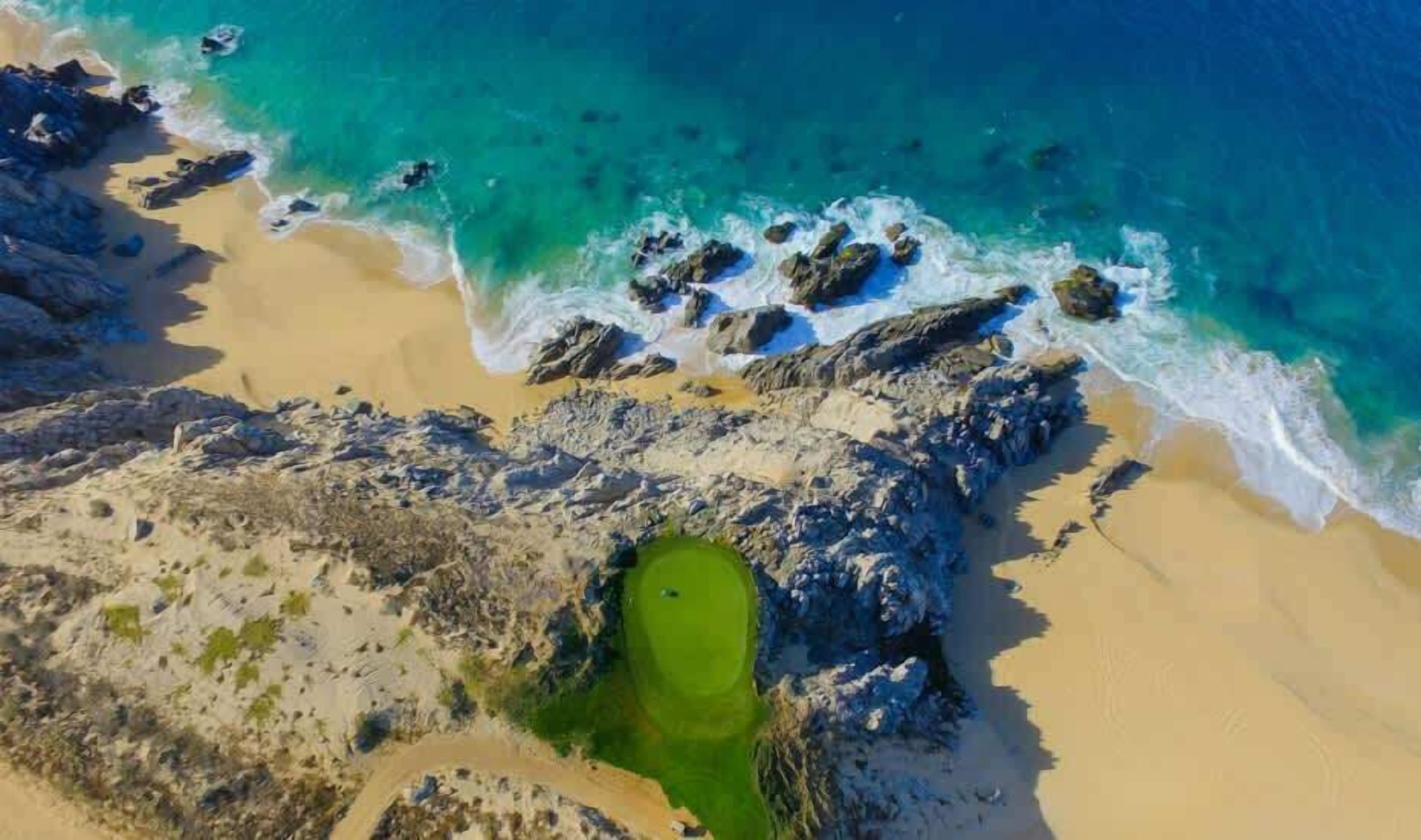 Paisagem costeira com praia, falésias rochosas e área verde.