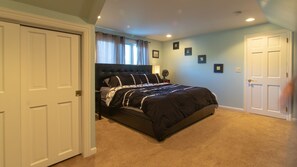 A bedroom with a large bed, two doors, a ceiling fan, and framed pictures on the wall.