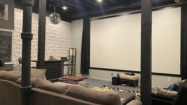 A modern living room with a large screen, comfortable seating, and a decorative wall.