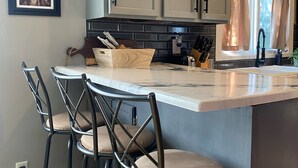 Una cocina con una isla central, taburetes de bar y cuadros en la pared.