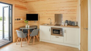 Eine kompakte Küche mit Holzboden, einem Flachbildfernseher, einem Spülbecken, einer Mikrowelle und einer kleinen Essecke mit Stühlen.
