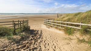 Ein Sandweg am Strand mit hölzernen Geländern, der zum Meer führt.