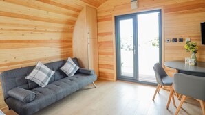 Ein gemütlicher Raum mit gewölbter Holzbalkendecke, einem grauen Sofa mit Karokissen, einem kleinen runden Tisch mit Stühlen und einer Glastür, die nach draußen führt.