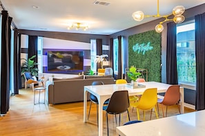 A modern living room with a flat-screen TV, a dining area with colorful chairs, a sofa, and a green wall with a #Together sign. - Stylish Clubhouse Retreat w/ Hot Tub near Downtown (Austin)