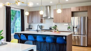Una cocina moderna con una isla central, taburetes de bar, electrodomésticos de acero inoxidable e iluminación colgante.