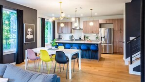 Una cocina moderna con armarios de madera, un refrigerador de acero inoxidable y un comedor con sillas coloridas.