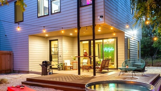 Una casa moderna con patio amueblado al aire libre, jacuzzi e iluminación con luces colgantes.