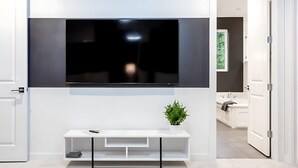 Una sala moderna con un televisor de pantalla plana montado en la pared, una consola blanca con una planta y una puerta que da a otra habitación.