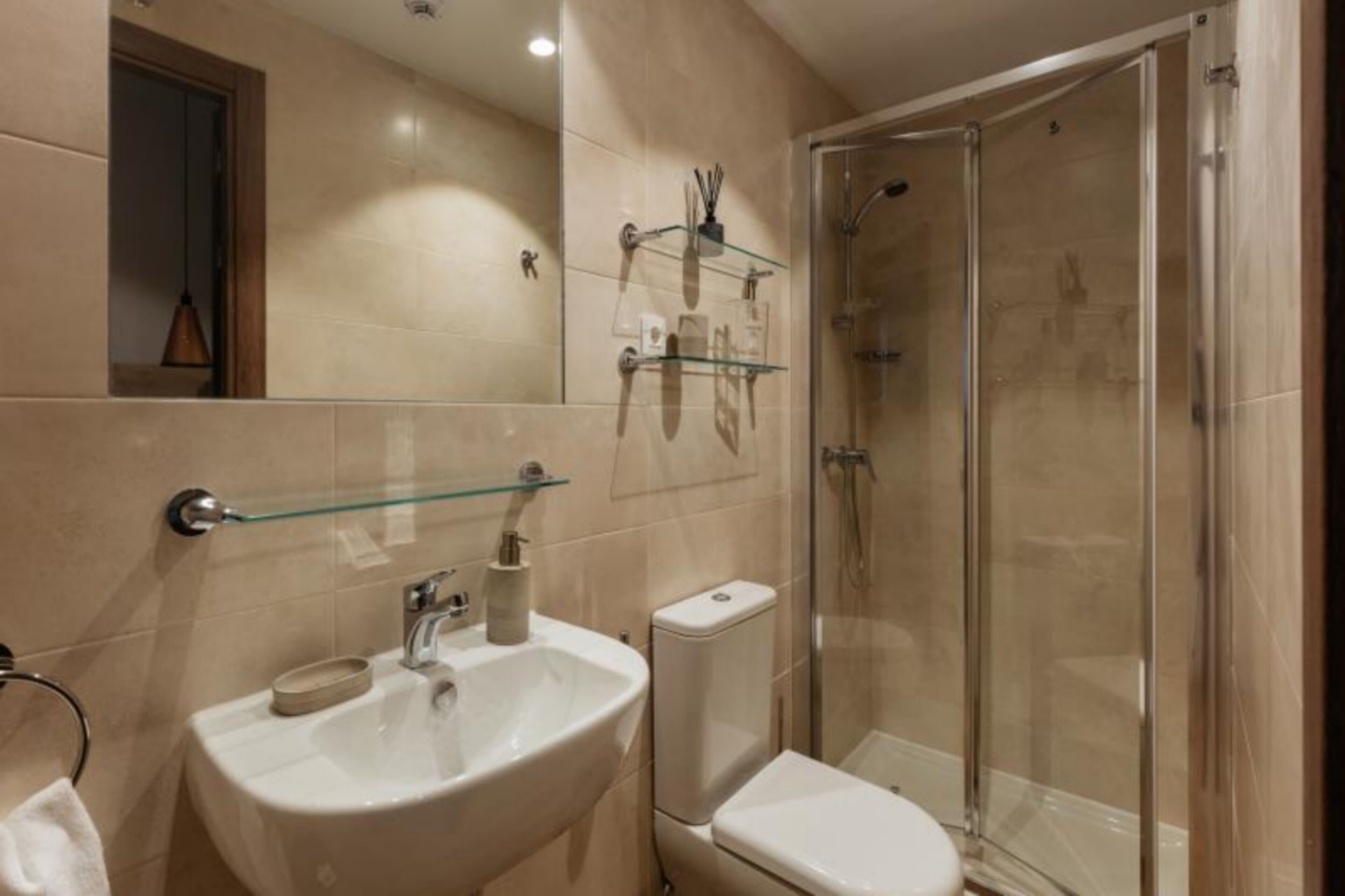 Un baño moderno con cabina de ducha de vidrio, un lavabo con repisa de vidrio arriba y un inodoro.