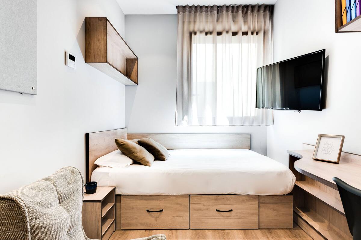 A modern bedroom with a bed, bedside table, TV, and a window with curtains.