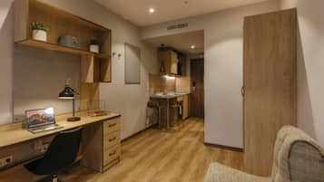 Ein kleines Zimmer mit einem Holztisch, einem Stuhl, einer kleinen Küchenzeile und einem Kleiderschrank.