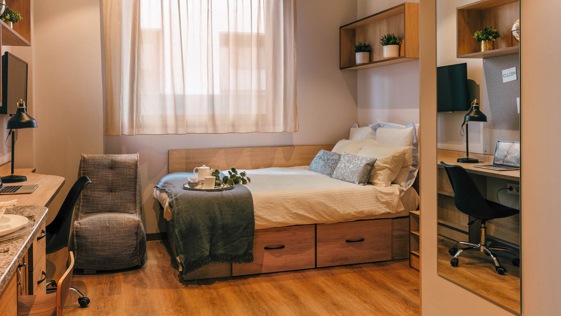 A compact bedroom with a bed, desk, chair, and a small shelf with plants.