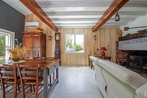 A rustic kitchen with wooden beams, a dining table, chairs, a clock, and a fireplace.