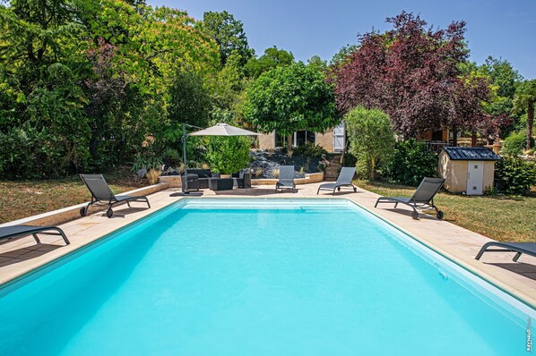 A rectangular swimming pool with lounge chairs and a small shed in a landscaped garden.