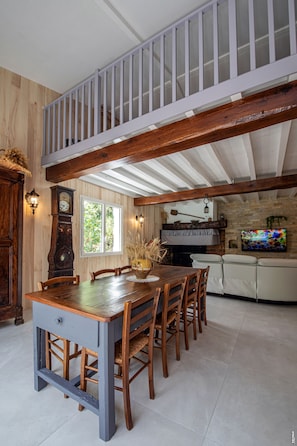 A dining area with a wooden table and chairs, a clock, and a television on a stone wall.