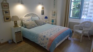 A bedroom with a bed, bedside tables, a chair, and a window with a view of trees. - Rez de Maison Avec Jardin Arboré Privatif à 1 km de la Plage (La Baule-Escoublac)