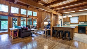 A spacious living room with a fireplace, a dining area, and a kitchen with wooden cabinets and a large window. - Quietside Cabin: Sunroom, Fire Pit, Theater Den, & Stunning Views (Walland)