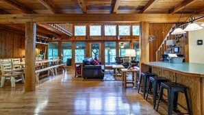 A spacious wooden interior with a high ceiling, large windows, a dining area, and a bar. - Quietside Cabin: Sunroom, Fire Pit, Theater Den, & Stunning Views (Walland)