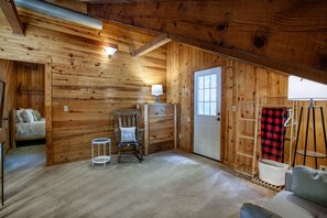 Ein gemütliches Holzhaus-Interieur mit einem Bett, einem Schaukelstuhl, einem kleinen Tisch und einer zur Außenseite führenden Tür.
