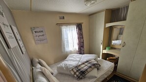 Ein kleines, gemütliches Schlafzimmer mit einem Einzelbett, einem Fenster mit Vorhängen, einem Spiegel und einem motivierenden Poster an der Wand.