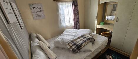 A small, cozy bedroom with a single bed, a window with curtains, a mirror, and a motivational poster on the wall.