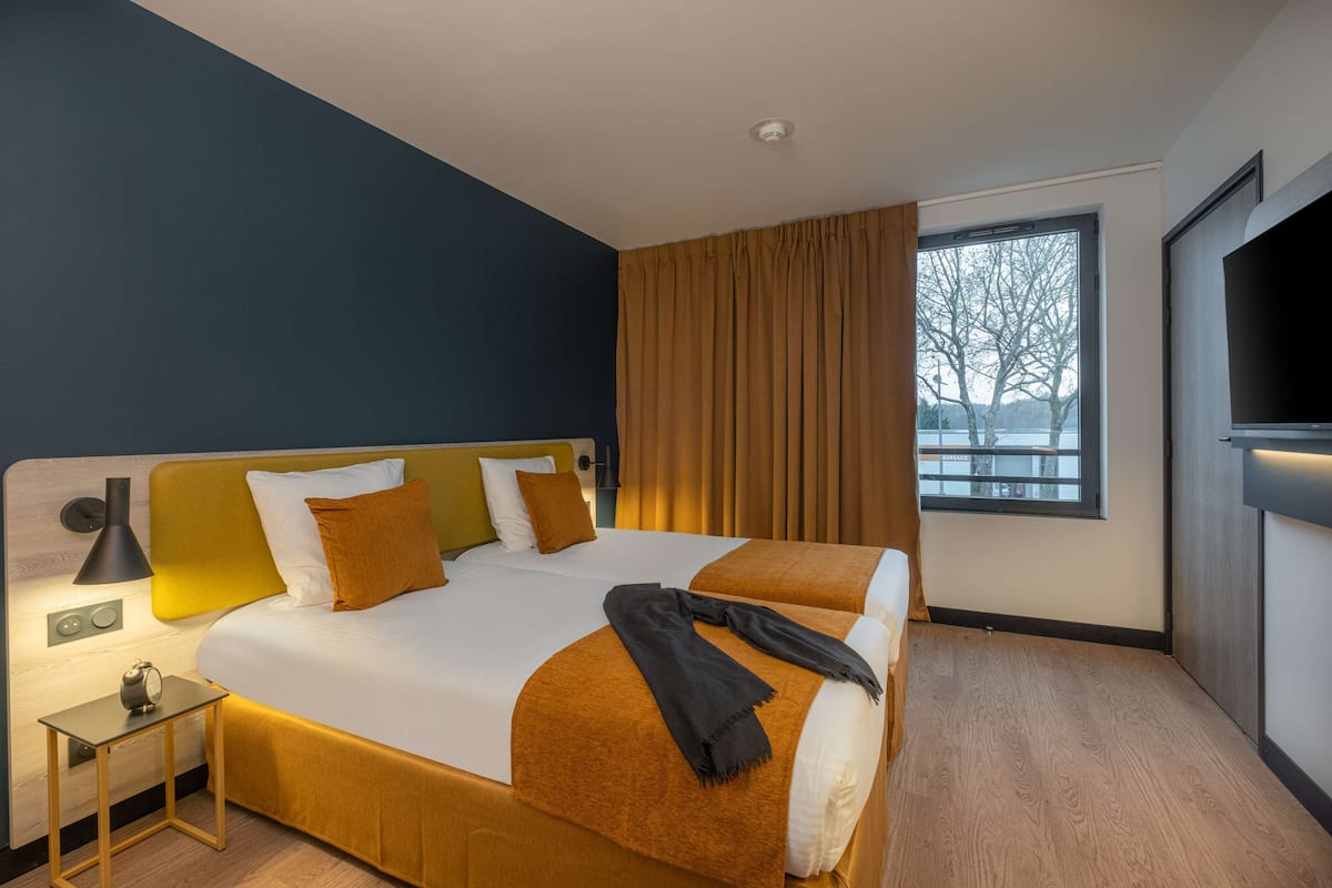 Une chambre d’hôtel avec un grand lit, une télévision, une fenêtre avec des rideaux et une table de chevet avec une lampe.