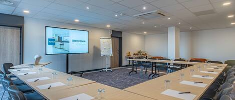A conference room with a long table, chairs, a projector screen, and a whiteboard.
