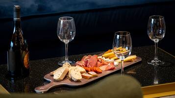 A table with a bottle of wine, two glasses, and a wooden board with various cheeses and meats.