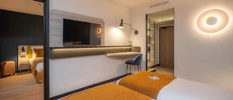 A modern hotel room with a bed, a desk, a chair, a TV, and a bathroom.