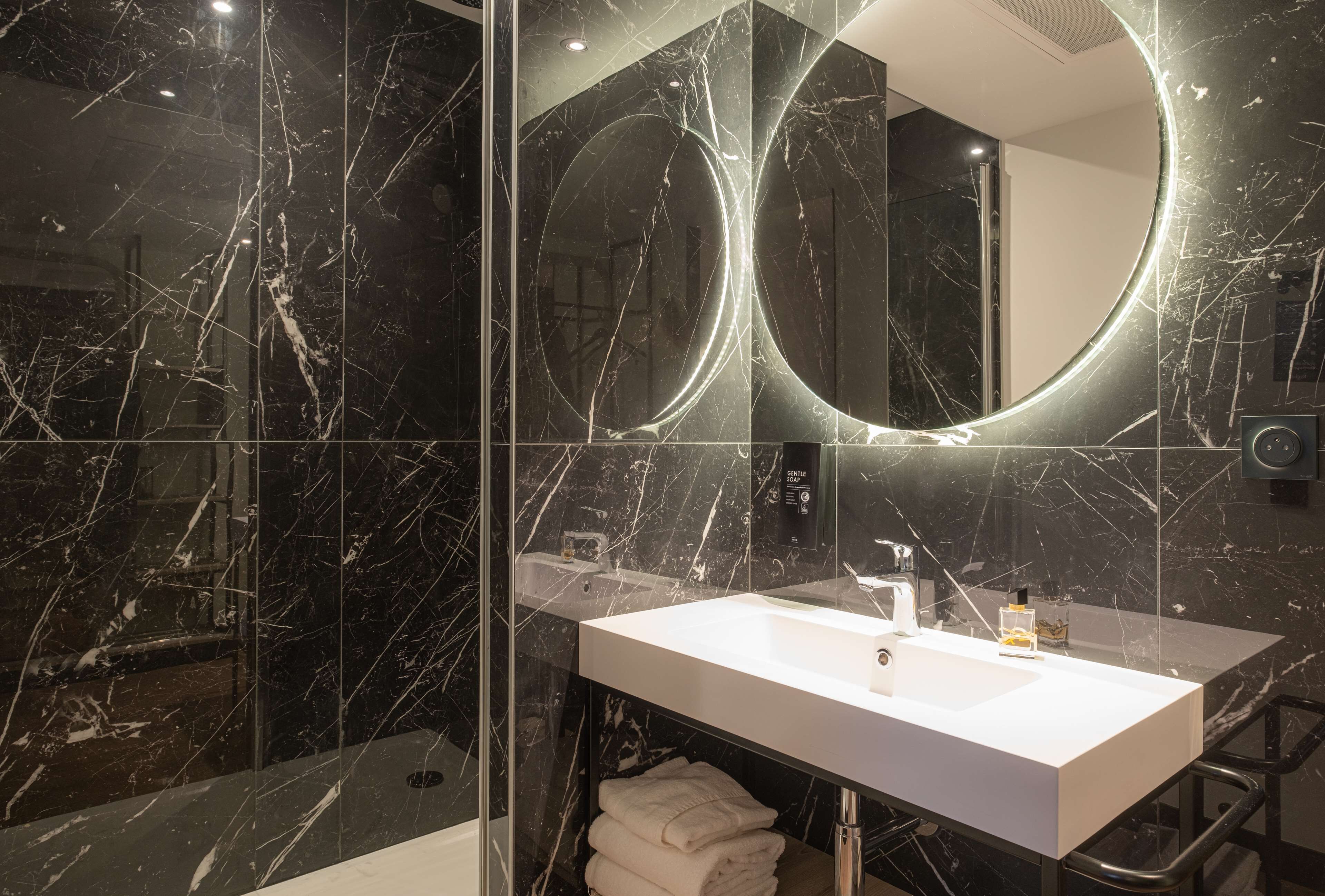A modern bathroom with a marble vanity, a large mirror, and a glass shower enclosure.