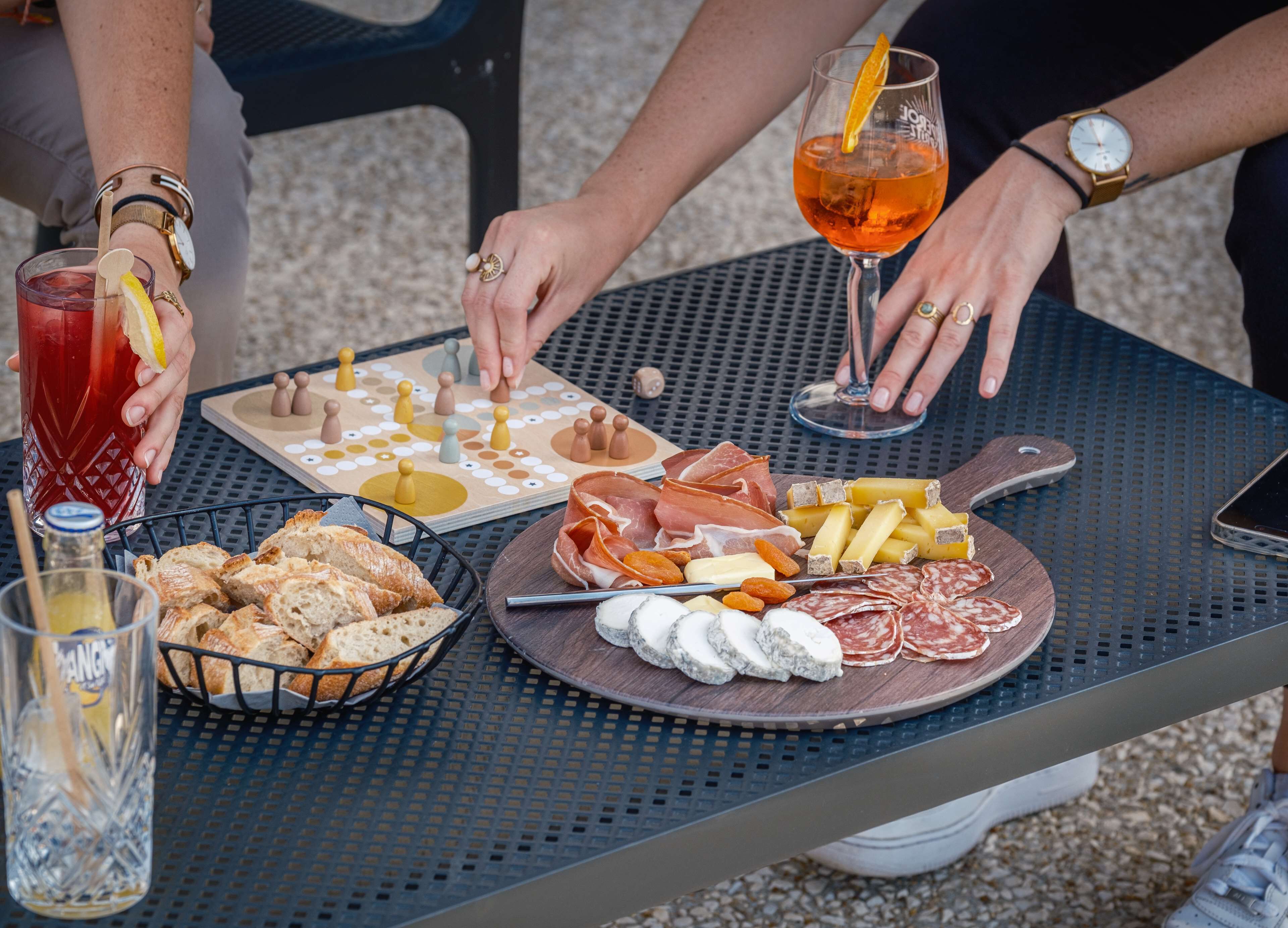 Una mesa con un juego de mesa, una tabla de quesos y fiambres, y bebidas.